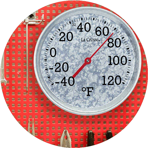 A silver round thermometer on a red pegboard wall with hand tools around it.